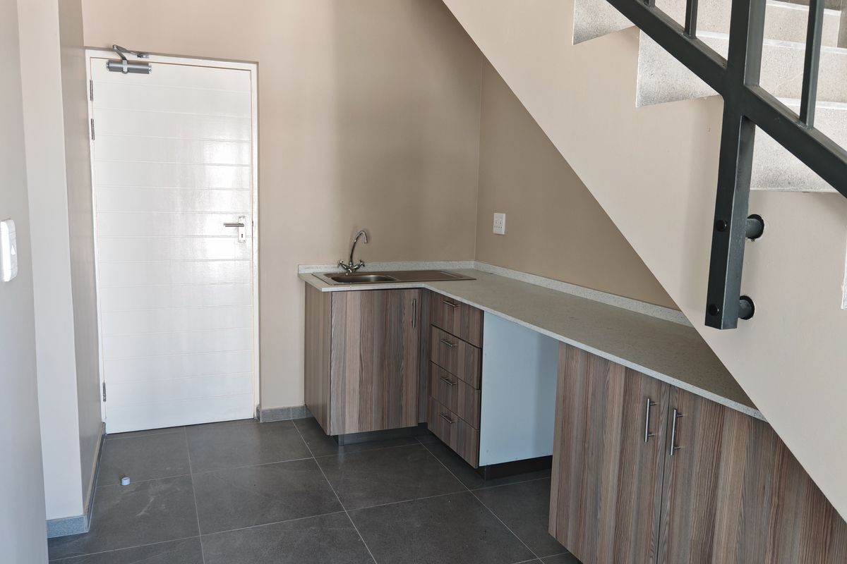 A functional kitchenette area located under the staircase, featuring built-in cabinetry, a sink, and tiled flooring.