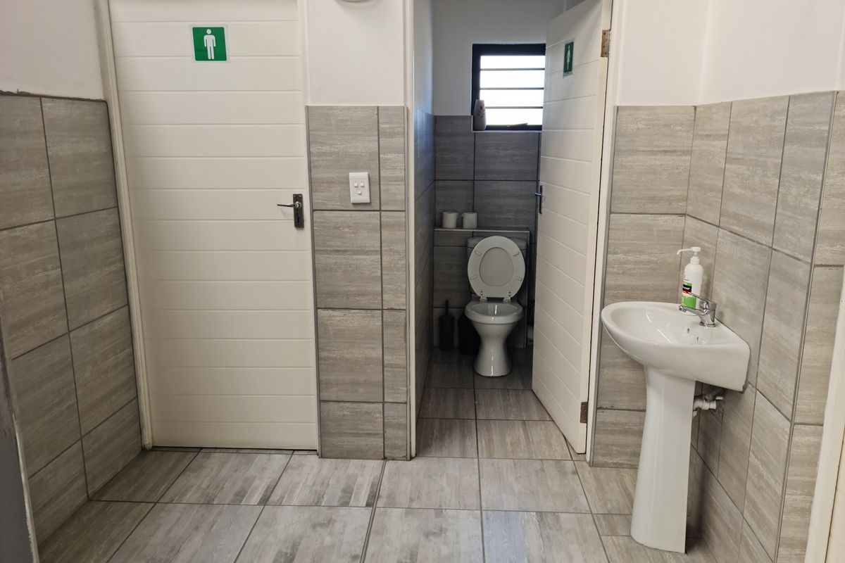A functional industrial restroom facility featuring tiled walls and flooring, a pedestal basin, and a private toilet cubicle.