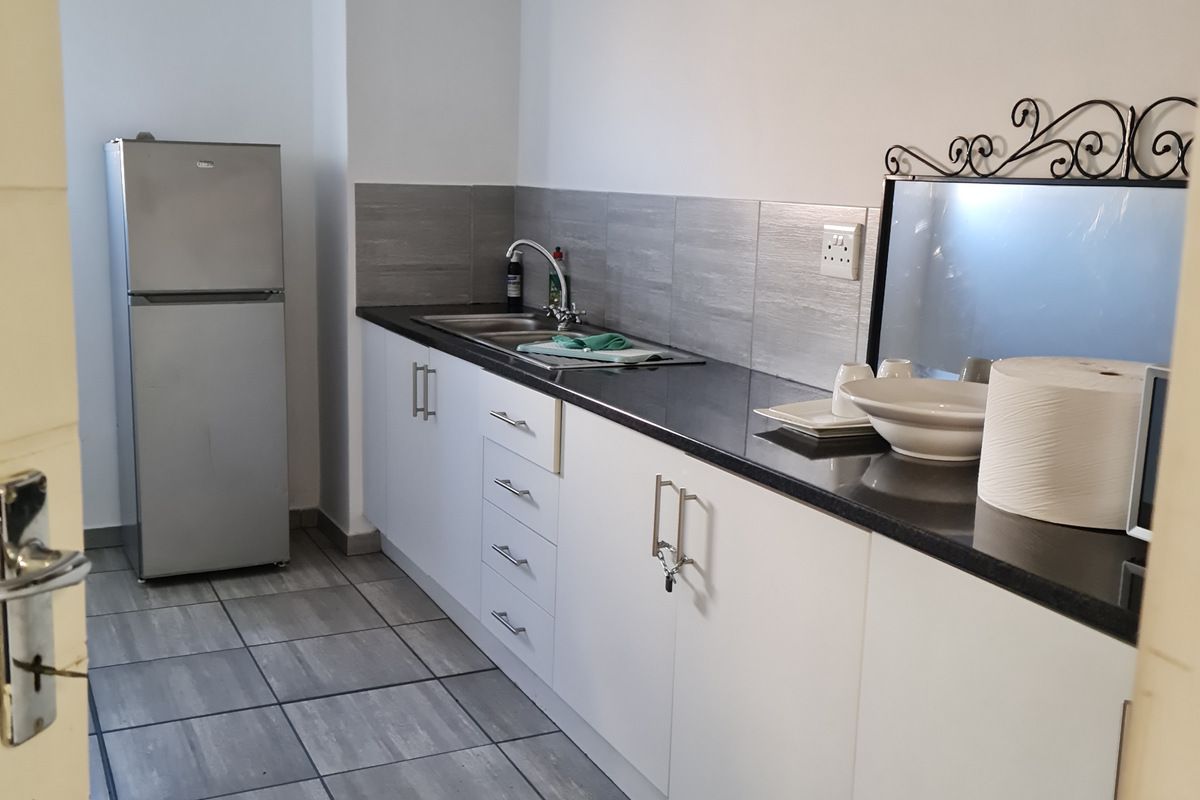 A compact kitchenette featuring white cabinetry, dark countertops, a stainless steel sink, and grey tiled flooring in an industrial-style space.