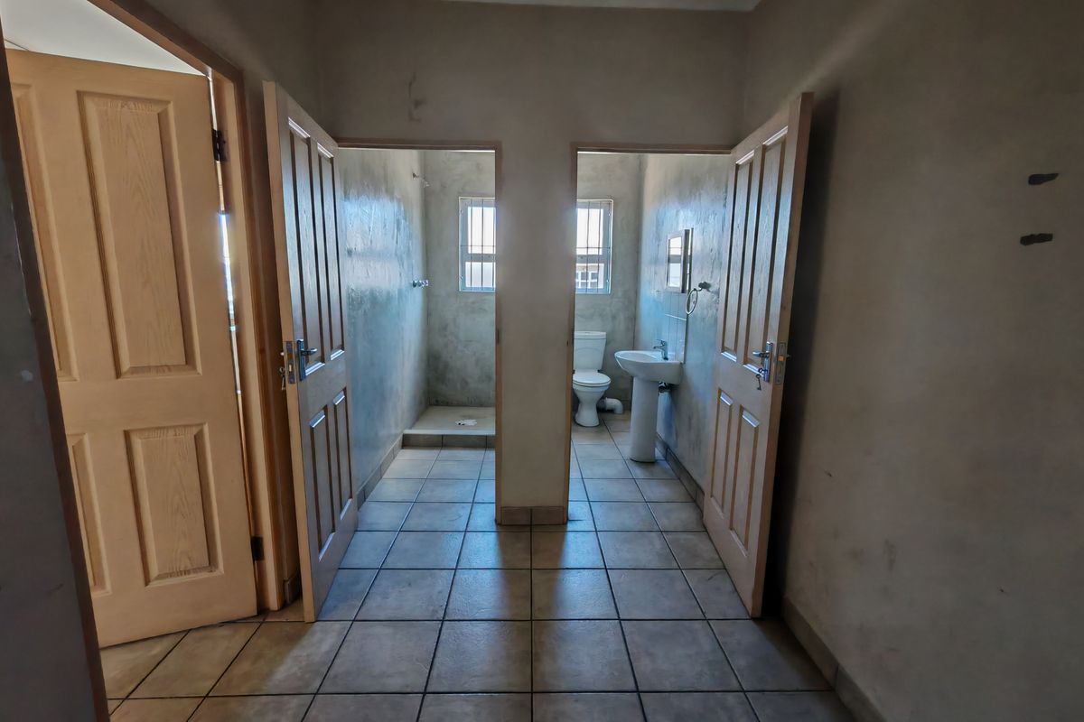 A functional industrial-style bathroom area featuring separate shower and toilet cubicles with tiled flooring and pedestal basin.