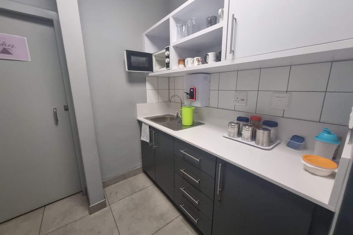 A compact kitchenette featuring dark grey base cabinetry, white upper shelving, a stainless steel sink, and tiled splashback.