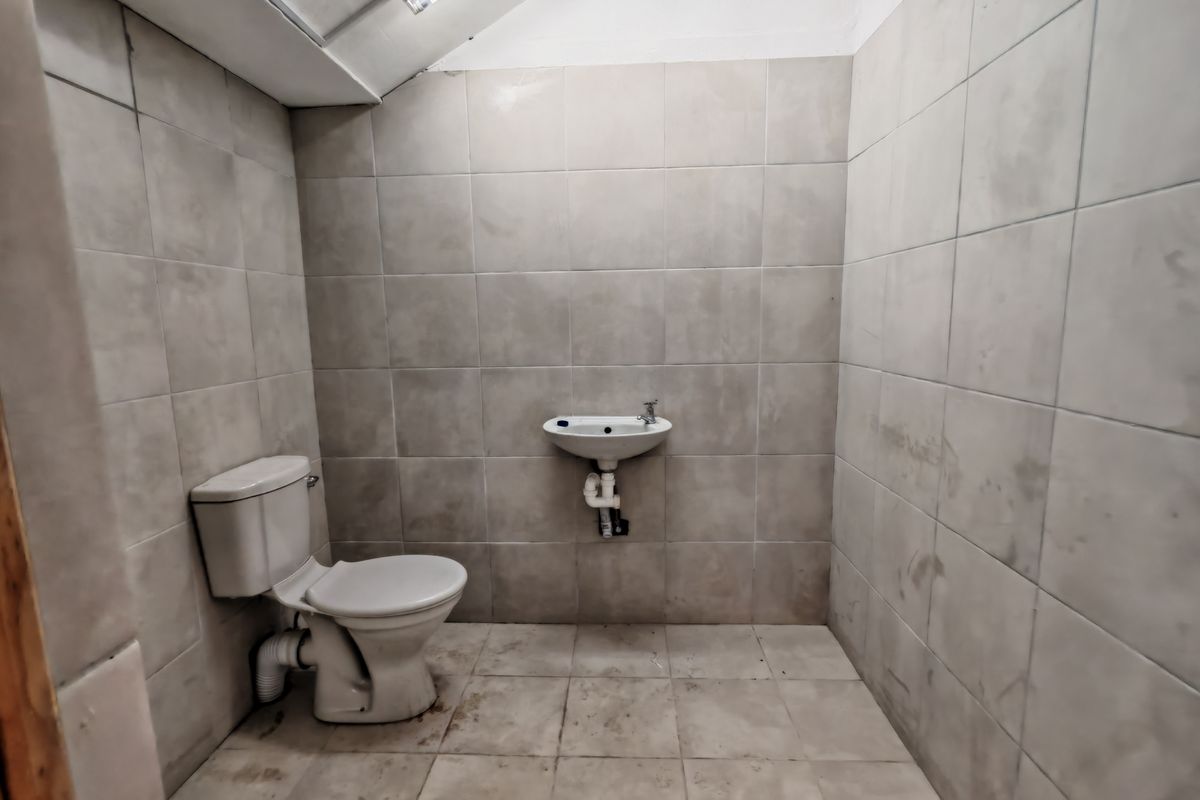 A functional industrial-style bathroom featuring tiled walls and flooring, equipped with a standard toilet and a wall-mounted basin.
