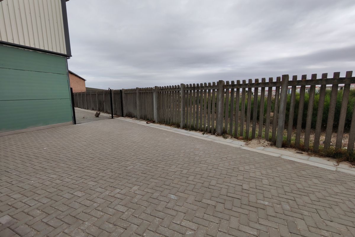 A paved outdoor area featuring a concrete palisade fence and industrial building cladding, providing a secure and functional exterior space.
