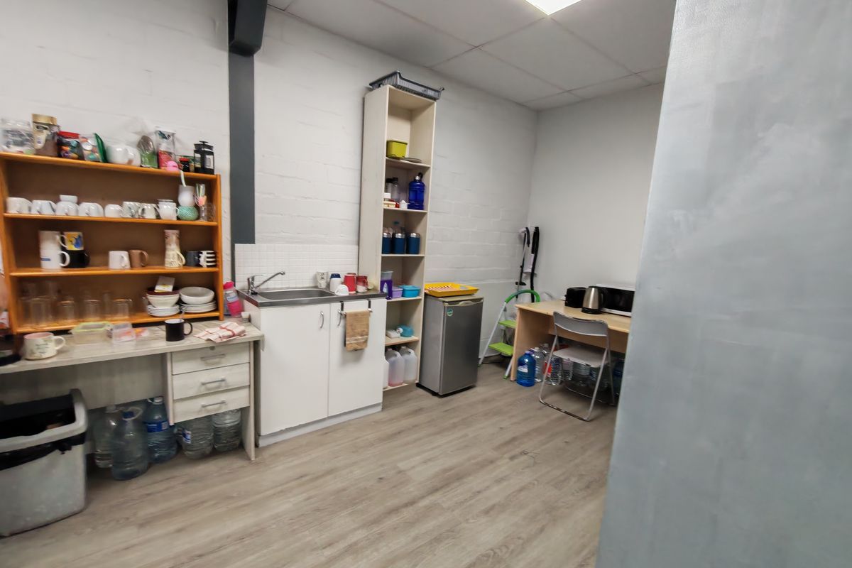 A functional office kitchenette area featuring a sink, built-in cabinetry, shelving, and wood-look flooring in a clean, utilitarian office space.