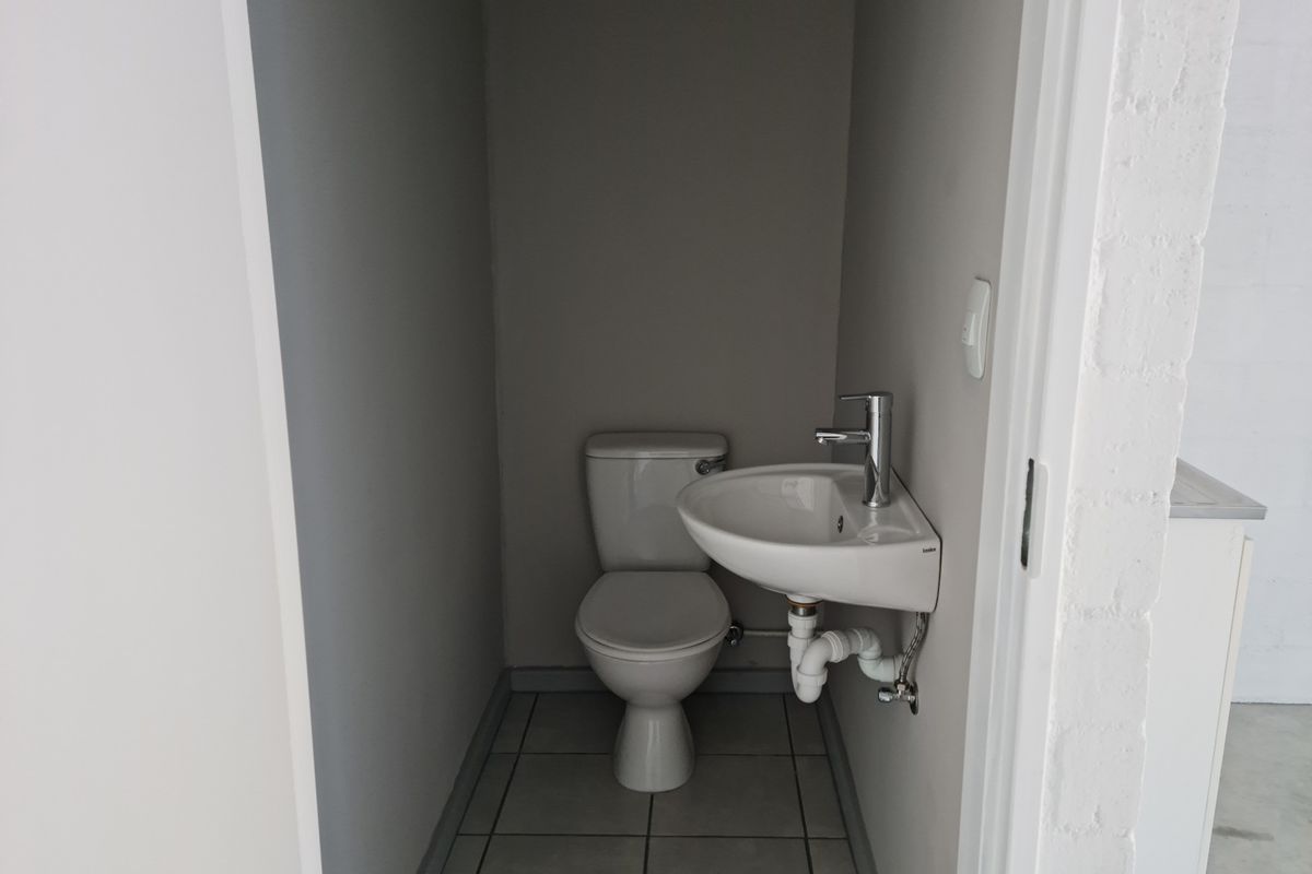 A compact industrial-style restroom featuring a wall-mounted basin and a standard toilet suite with tiled flooring.