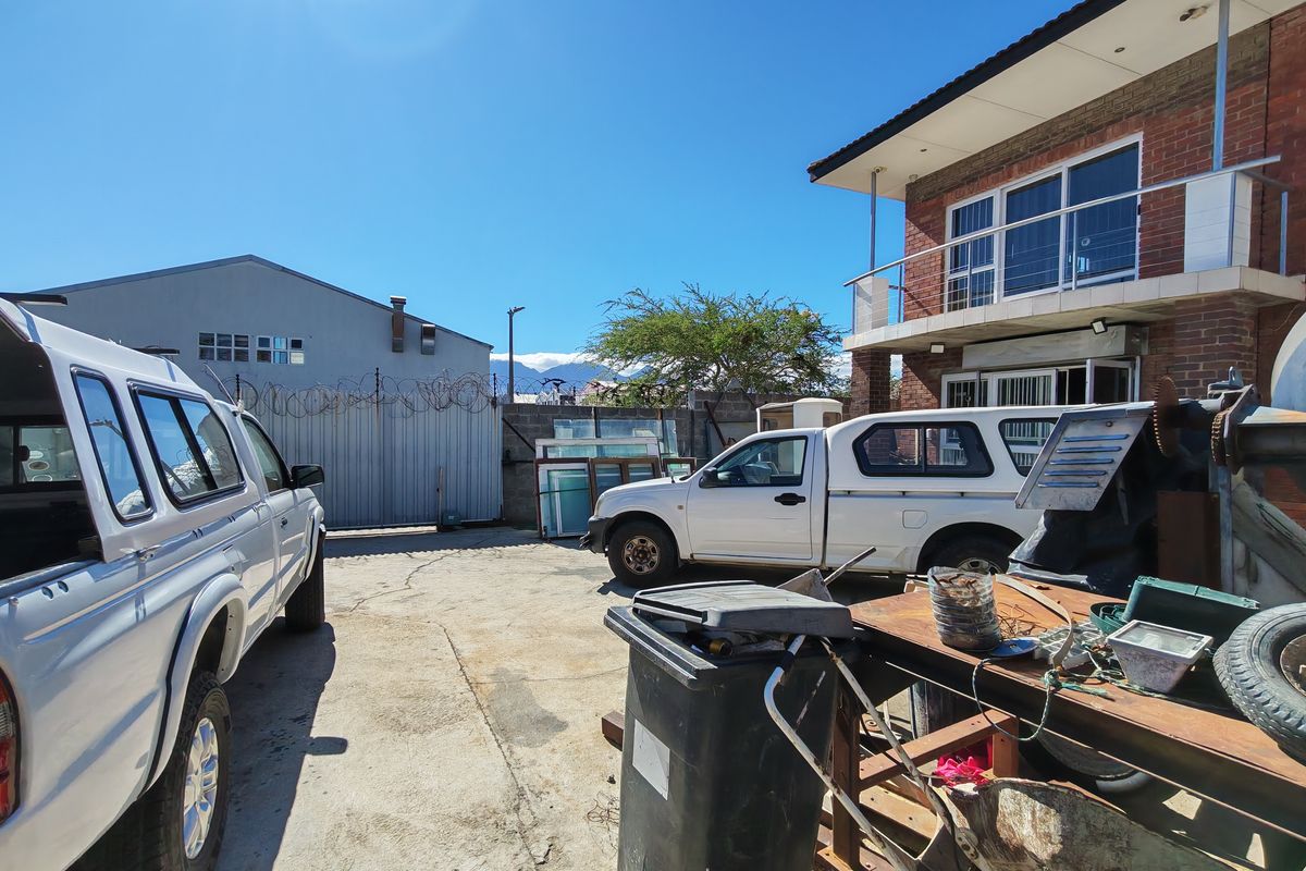 Exterior view of an industrial property yard featuring concrete paving, perimeter fencing with razor wire, and a multi-story brick building structure.
