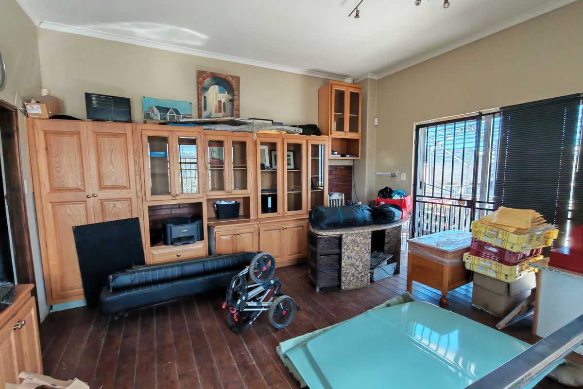 A versatile room featuring extensive built-in wooden cabinetry, timber flooring, and direct access to an outdoor area through a security-gated glass door.