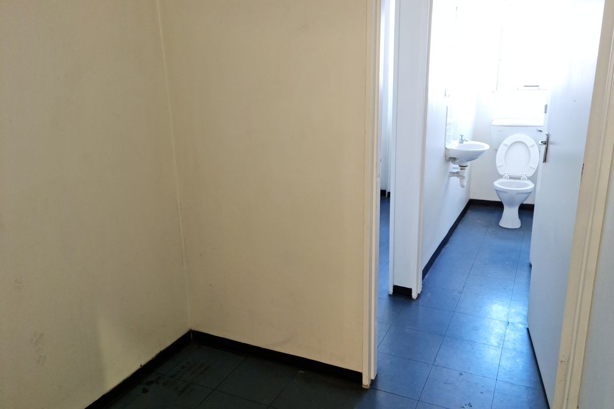 A functional industrial restroom facility featuring a standard toilet and wall-mounted basin with tiled flooring.