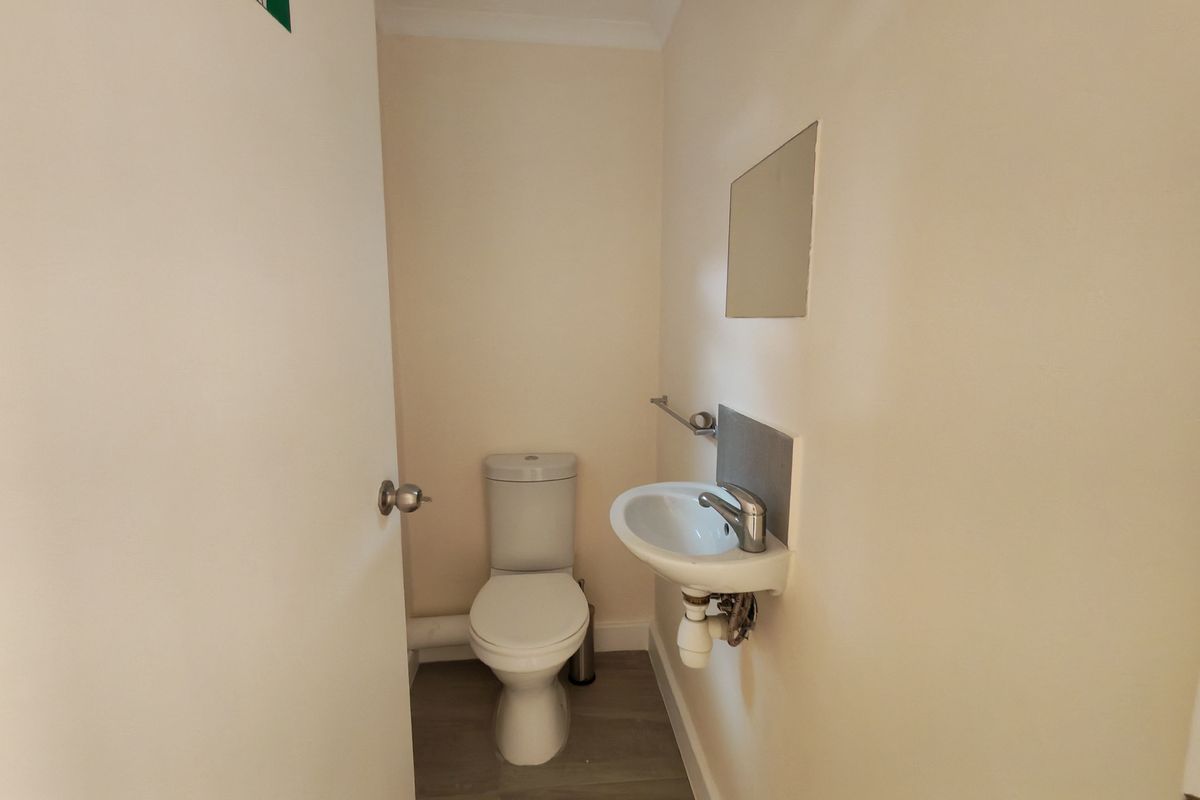 A compact industrial restroom featuring a standard toilet, wall-mounted basin with chrome faucet, and neutral finishes.
