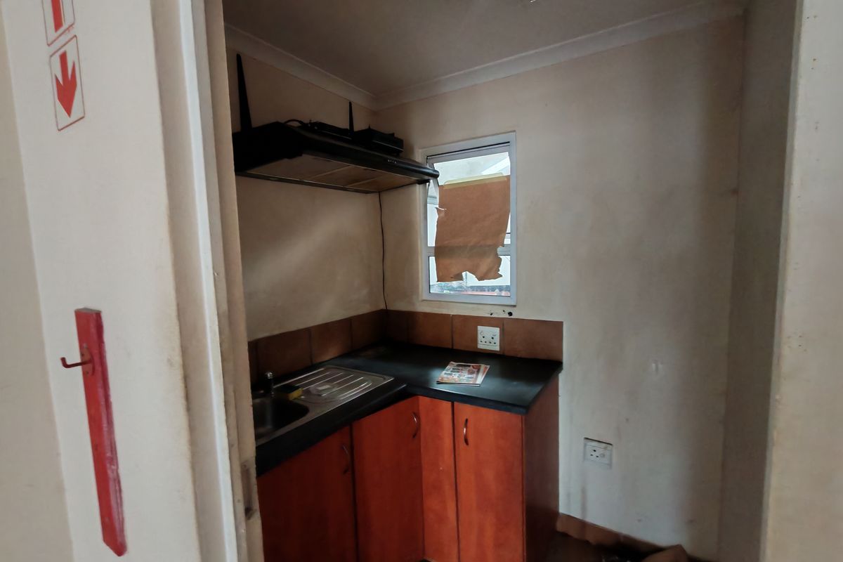 Compact kitchenette featuring built-in cabinetry, a stainless steel sink, and an extractor fan, suitable for a small industrial office or utility space.