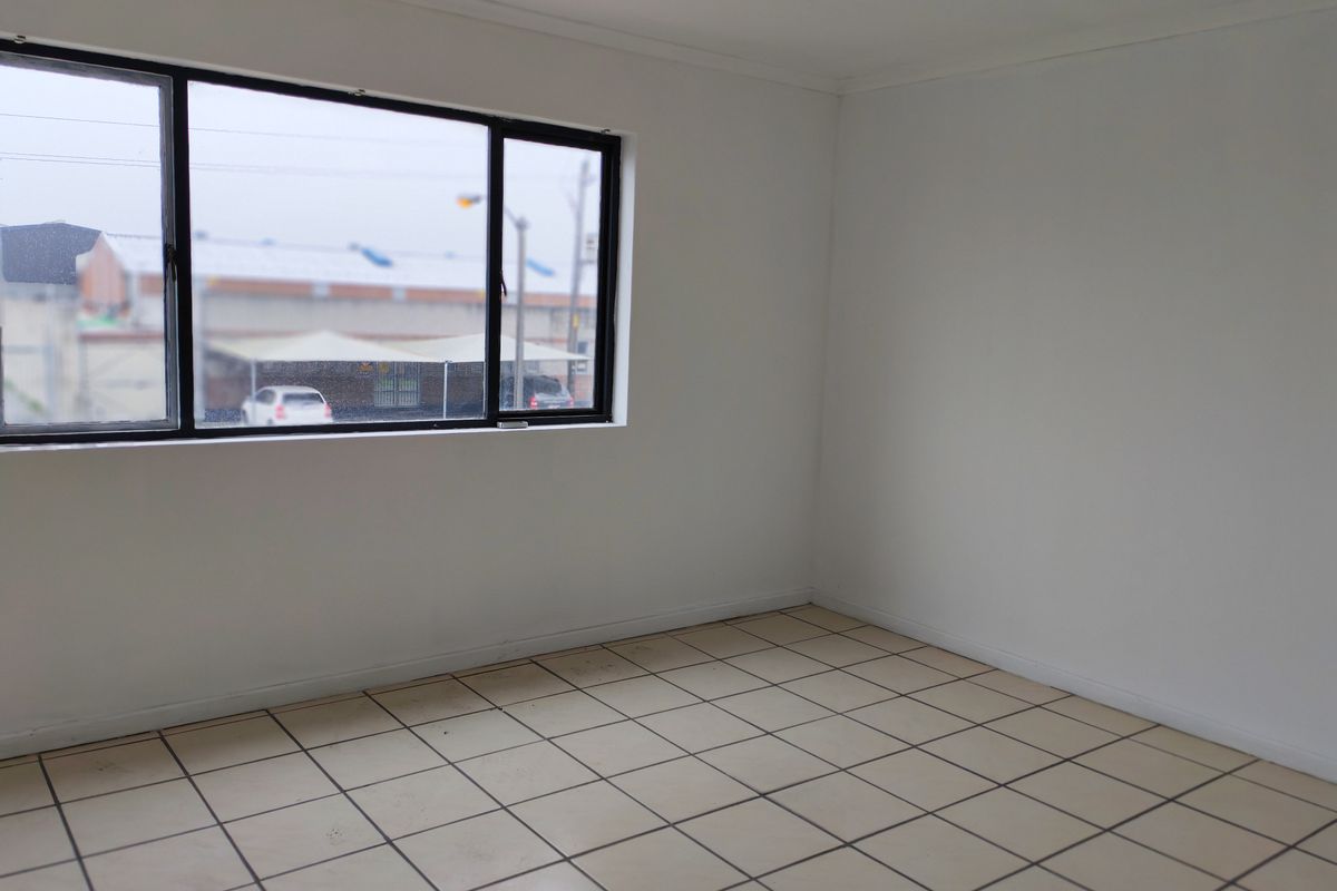 A vacant, neutral-toned room featuring tiled flooring and a large window, offering a blank canvas suitable for various industrial or office uses.
