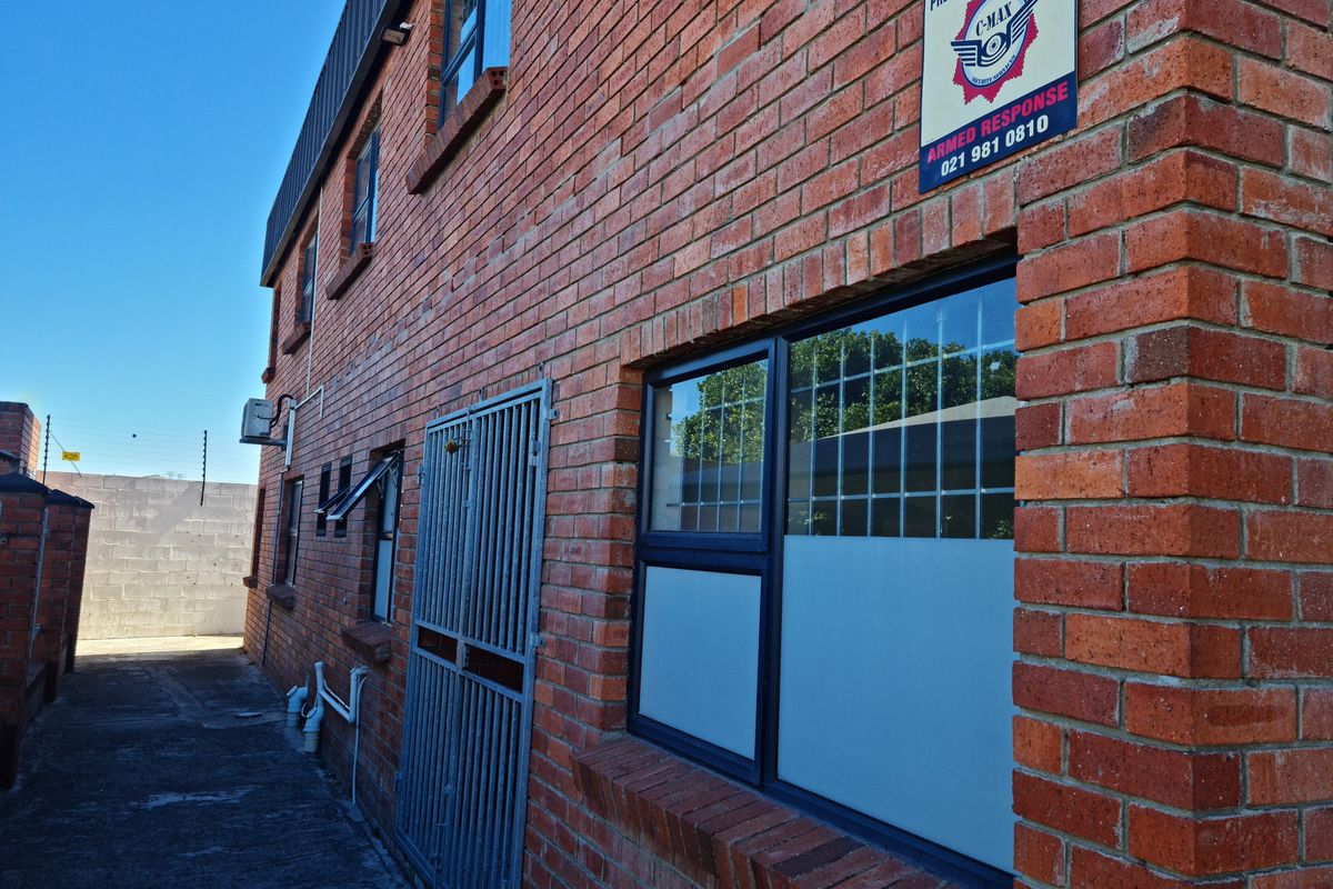 Side exterior view of the industrial brick building featuring security bars on windows, a metal security gate, and perimeter walling.