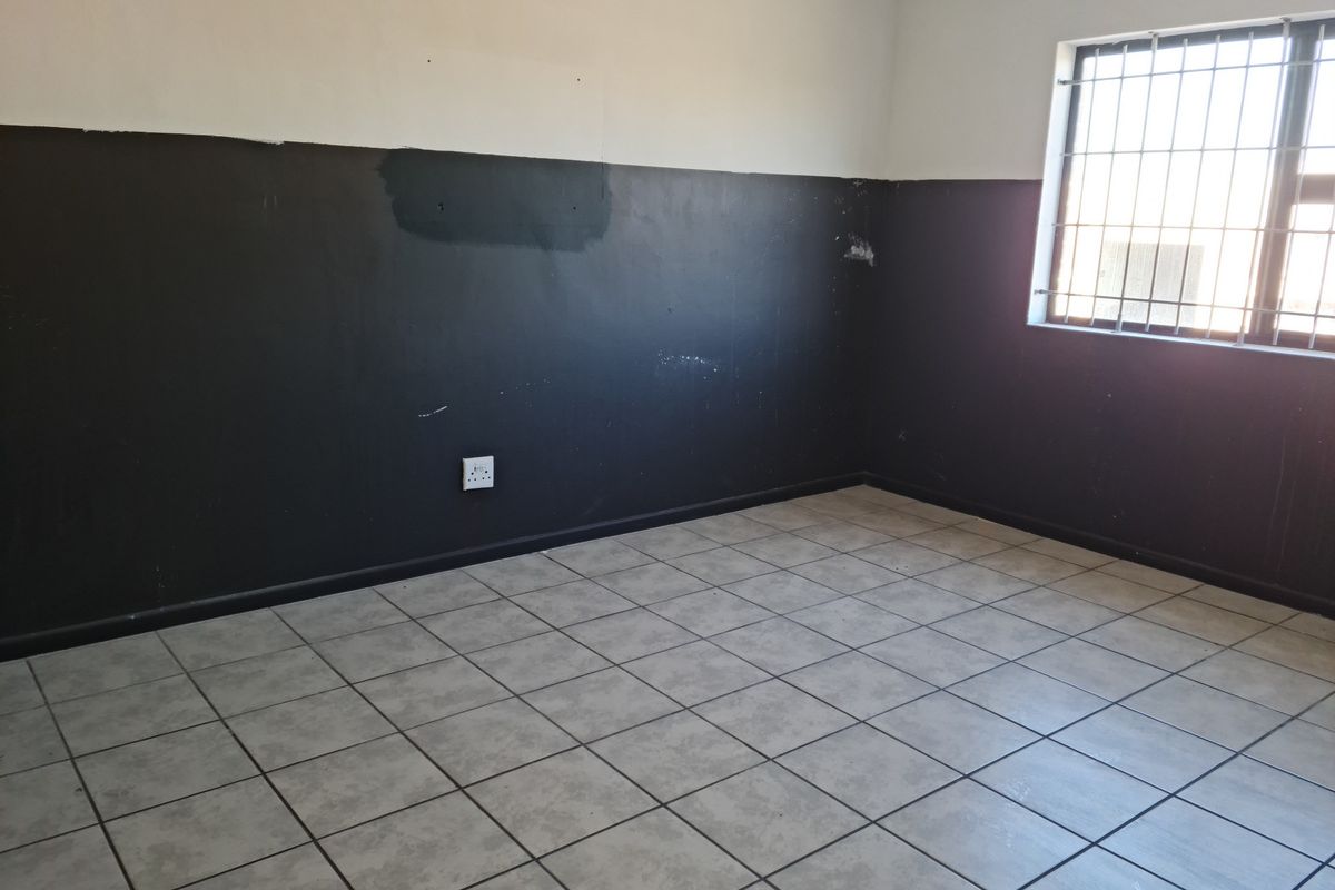 An empty room featuring tiled flooring and a window with security bars, characterized by a two-tone wall finish requiring cosmetic attention.