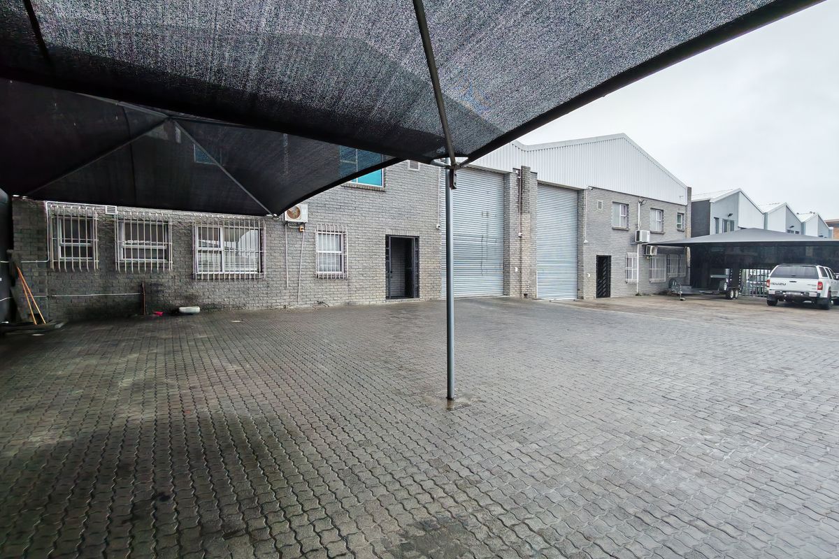 Industrial exterior yard featuring paved parking area, shade cloth canopy, and multiple roller shutter doors for warehouse access.
