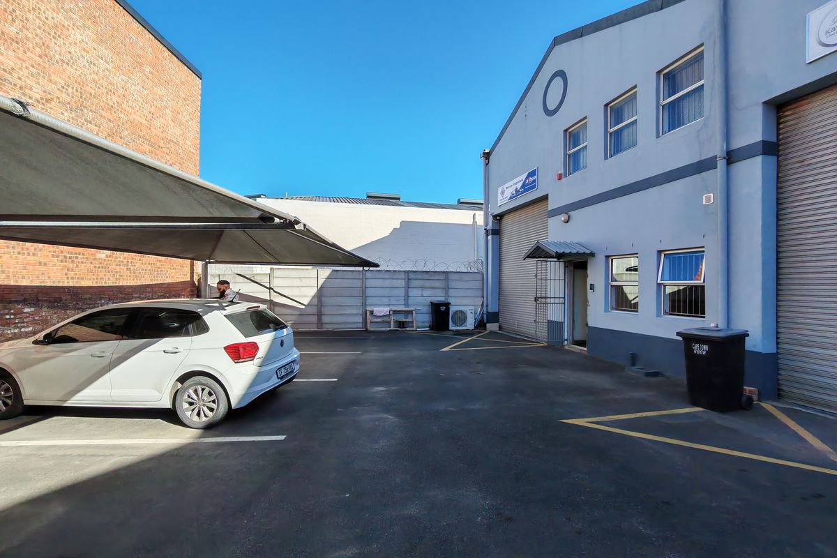 Industrial property exterior featuring a paved parking area, shade sail structure, and roller shutter door access to the warehouse facility.