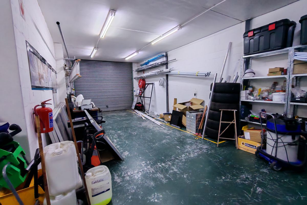 Industrial garage space featuring a roller shutter door, fluorescent lighting, and painted concrete flooring, suitable for storage or workshop use.