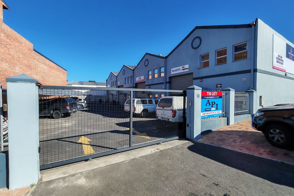 Industrial property exterior featuring a secure gated entrance, paved parking area, and multi-unit warehouse facade with roller shutter doors.