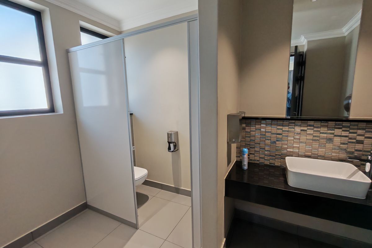 Modern office restroom featuring a vessel sink, granite countertop, mosaic tile backsplash, and a private toilet cubicle with partition.