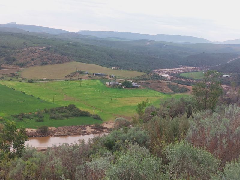 An elevated aerial view of a rural farm property featuring expansive green pastures, a river, and surrounding mountainous landscape.