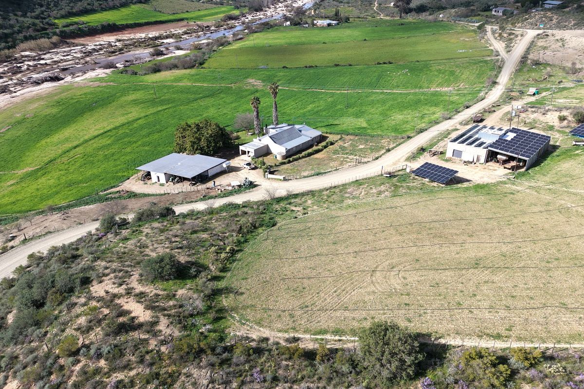 Aerial view of a rural farm property featuring multiple outbuildings, solar panel installations, and extensive agricultural land with river access.