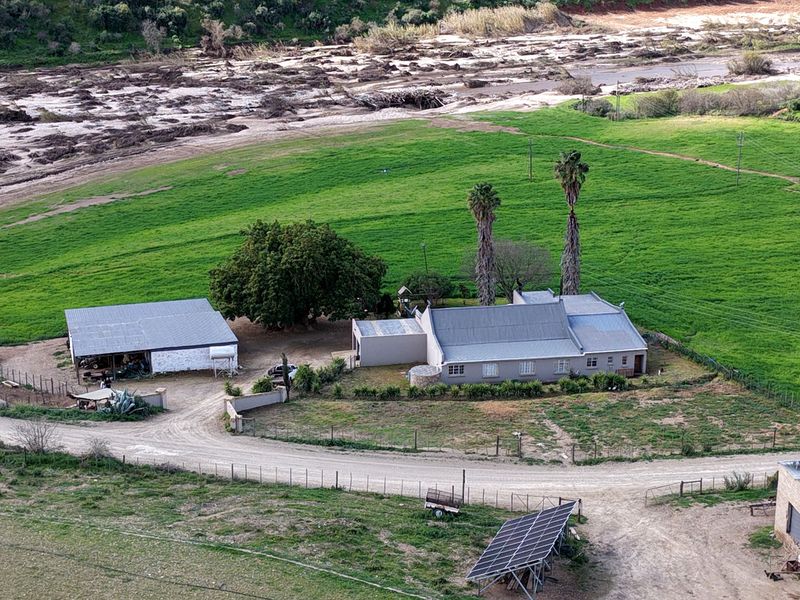 Aerial view of a farm property featuring a main dwelling, an outbuilding, a solar panel array, and surrounding green fields near a riverbed.