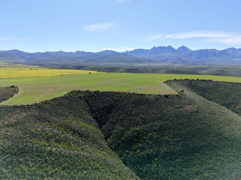 An expansive aerial view of the farm property featuring rolling green agricultural fields and a scenic mountain range backdrop.