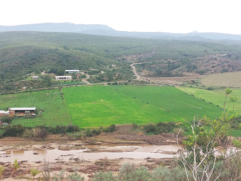 An elevated aerial view of the farm property, showcasing expansive green pastures, a river, a dam, and surrounding rural landscape.