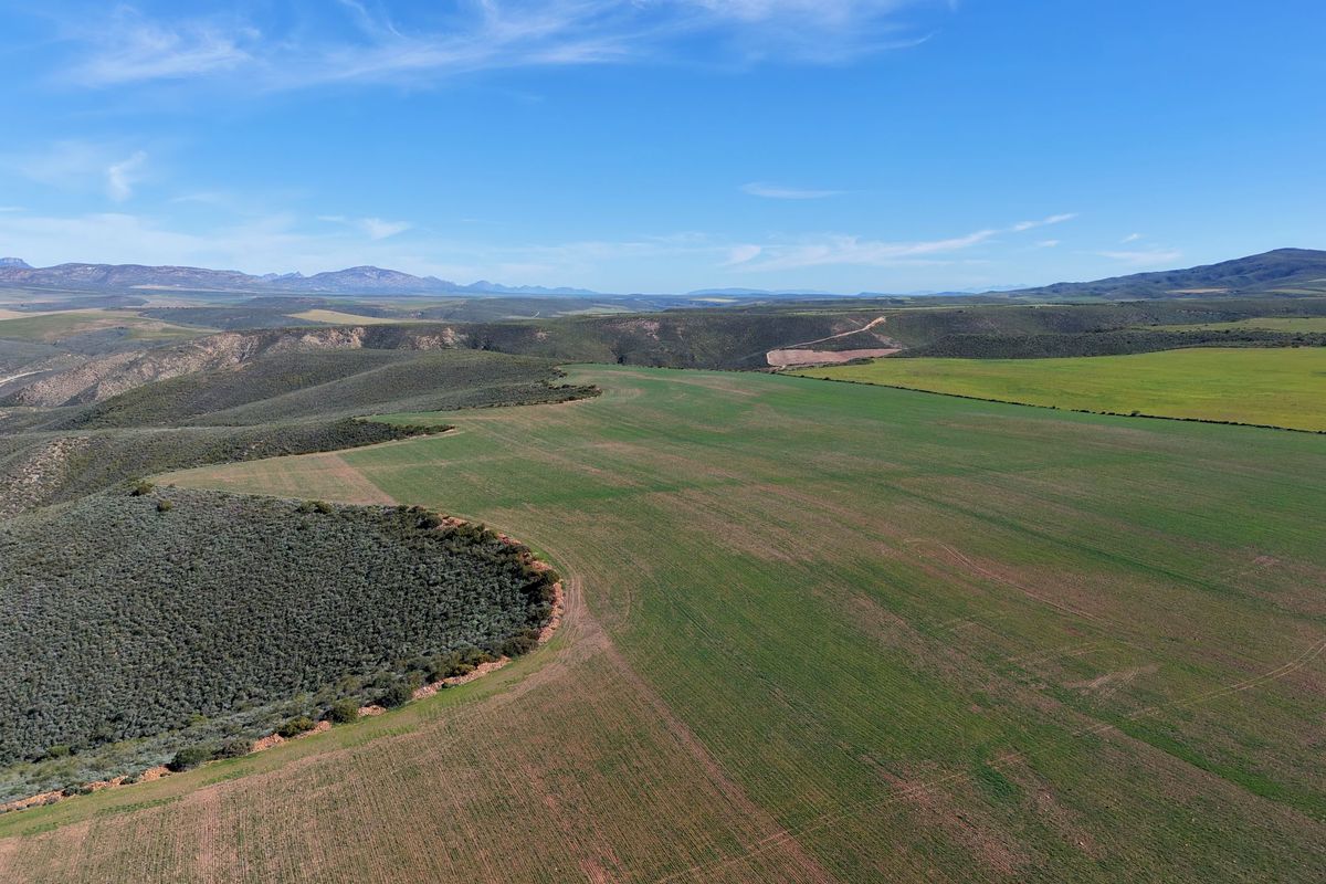 An expansive aerial view of the farm property, showcasing vast cultivated fields and natural rolling landscape under a clear blue sky.