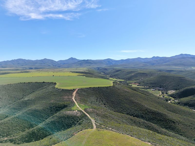 An expansive aerial view of the farm property, showcasing rolling hills, agricultural fields, and a dirt access road under a clear blue sky.