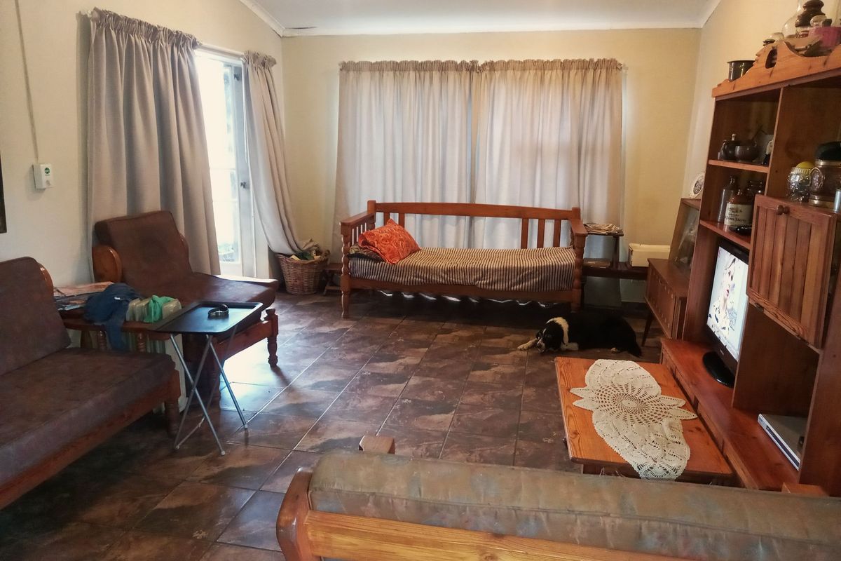 A spacious living room featuring tiled flooring and large windows with curtains, providing access to the outdoor area.
