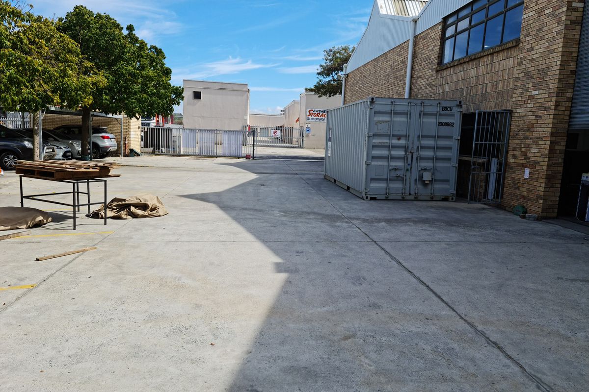 A spacious industrial concrete yard area featuring brick building facades, secure gated access, and metal cladding, suitable for storage or operational use.
