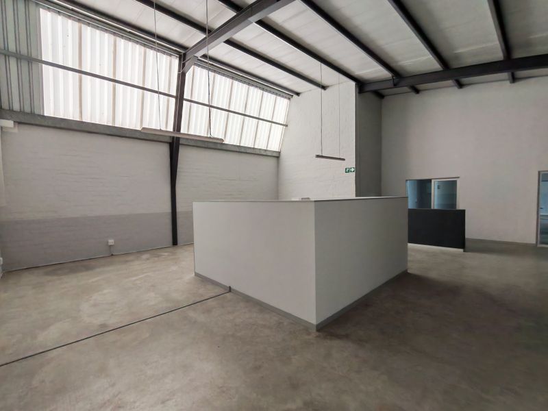 Spacious open-plan office area featuring high ceilings with exposed steel beams, polished concrete floors, and large clerestory windows providing ample natural light.
