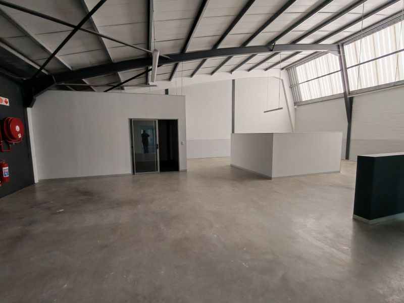 Spacious open-plan office area featuring high ceilings with exposed steel trusses, polished concrete floors, and natural light from overhead skylights.
