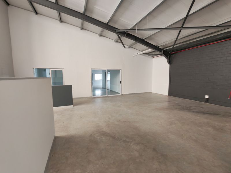 Spacious open-plan office area featuring high ceilings with exposed steel trusses, polished concrete floors, and modern glass partition doors.