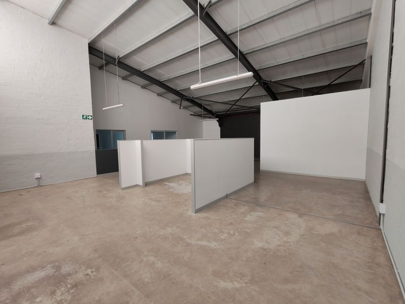Spacious open-plan office area featuring exposed steel roof trusses, concrete flooring, and modular partition walls, providing a versatile workspace environment.