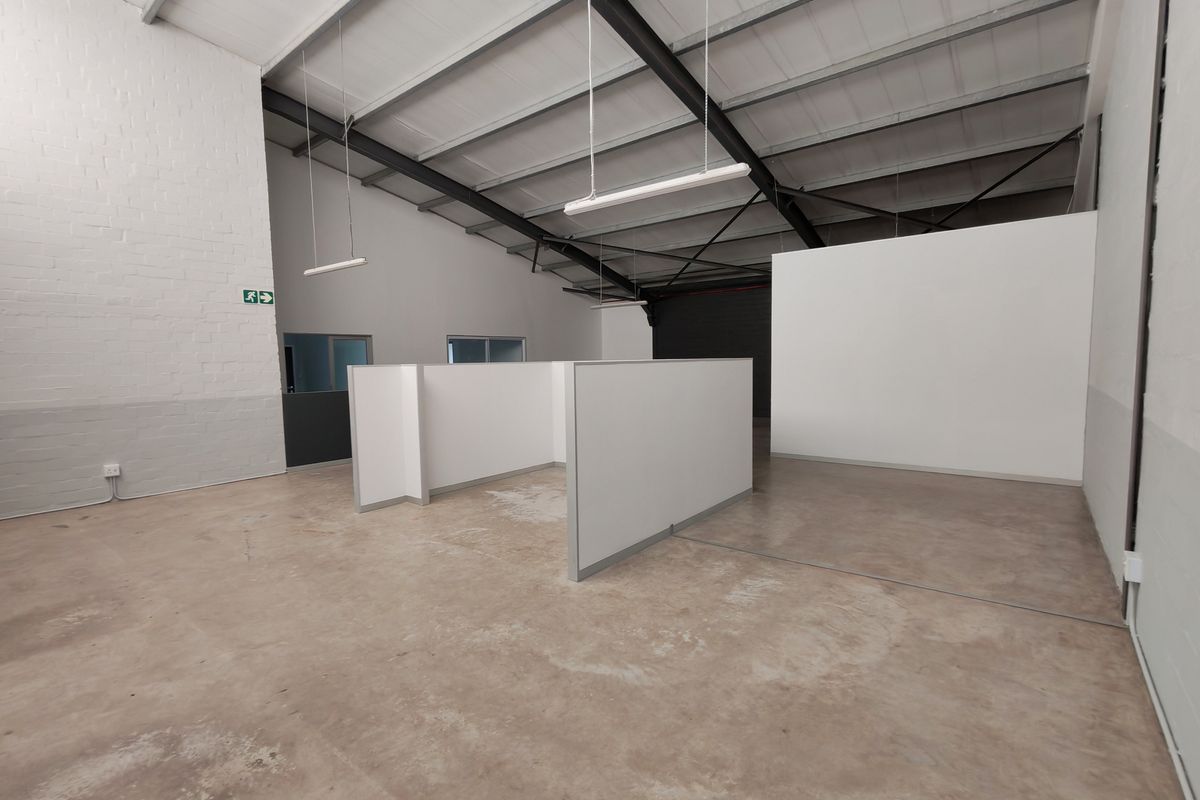 Spacious open-plan office area featuring exposed steel roof trusses, concrete flooring, and modular partition walls, providing a versatile workspace environment.