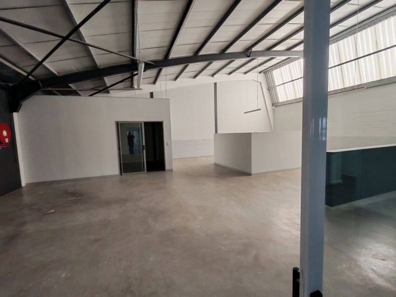 Spacious open-plan office area featuring polished concrete floors, exposed steel roof trusses, and natural light from translucent roof panels.