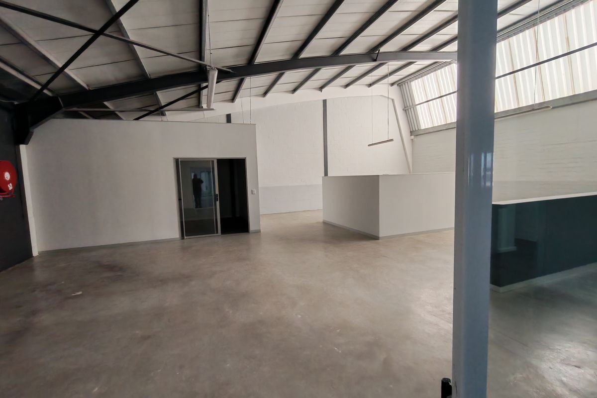 Spacious open-plan office area featuring polished concrete floors, exposed steel roof trusses, and natural light from translucent roof panels.