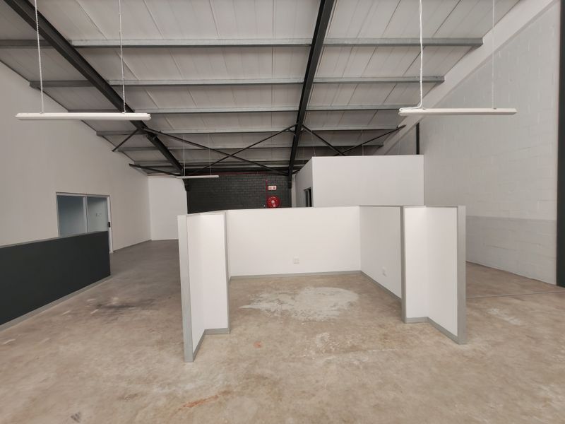 Open-plan office space featuring high exposed steel roof trusses, concrete flooring, and modular partition walls, offering a versatile industrial-style workspace.
