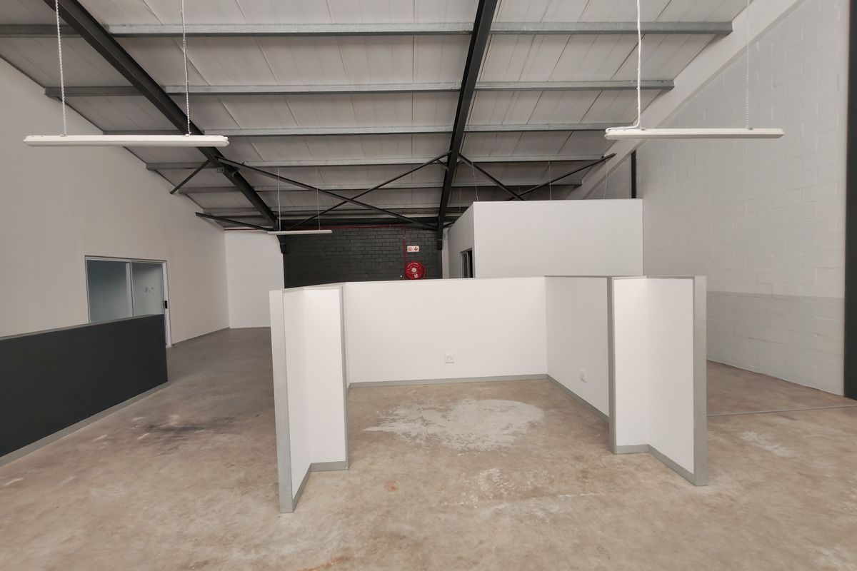 Open-plan office space featuring high exposed steel roof trusses, concrete flooring, and modular partition walls, offering a versatile industrial-style workspace.