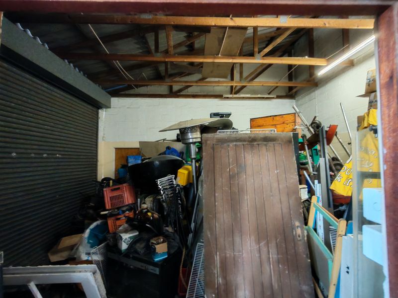Industrial garage space featuring exposed timber roof trusses, concrete block walls, and a roller shutter door, currently used for storage.