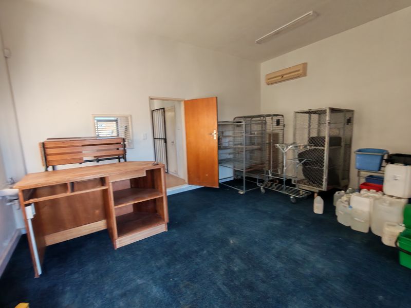 A functional utility space featuring carpet flooring, a wall-mounted air conditioning unit, and a security gate, suitable for storage or administrative use.