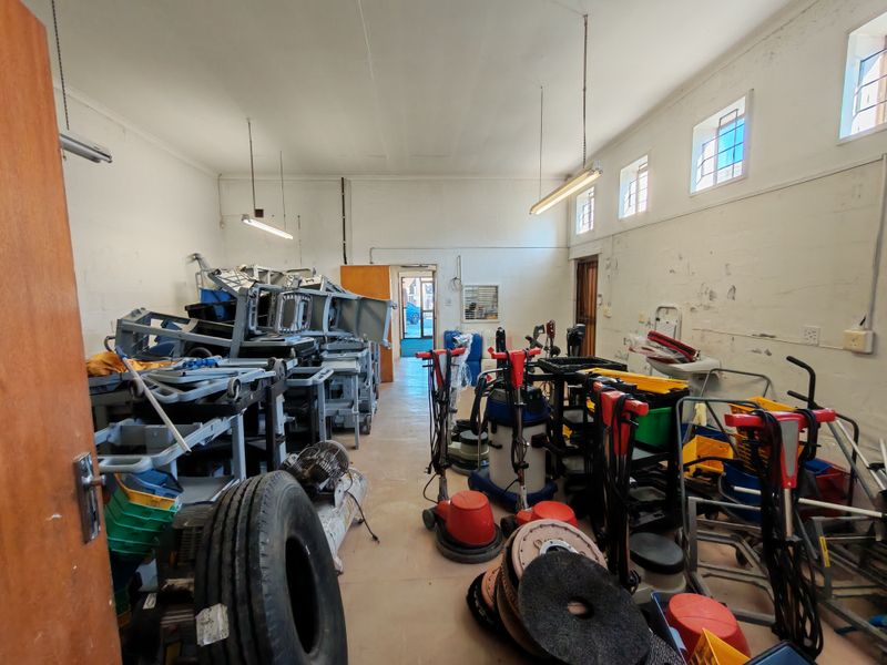 A functional industrial utility space featuring high-level windows, fluorescent lighting, and exposed masonry walls, currently utilized for storage.