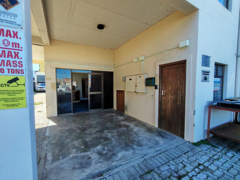 Industrial building entrance featuring a sliding glass door, a solid wooden door, and an exposed concrete ceiling with visible exterior wall wear.