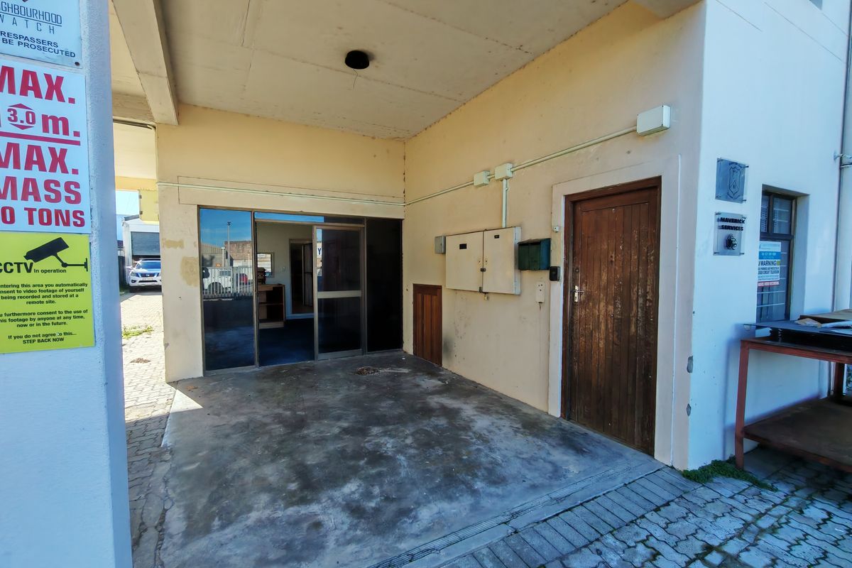 Industrial building entrance featuring a sliding glass door, a solid wooden door, and an exposed concrete ceiling with visible exterior wall wear.