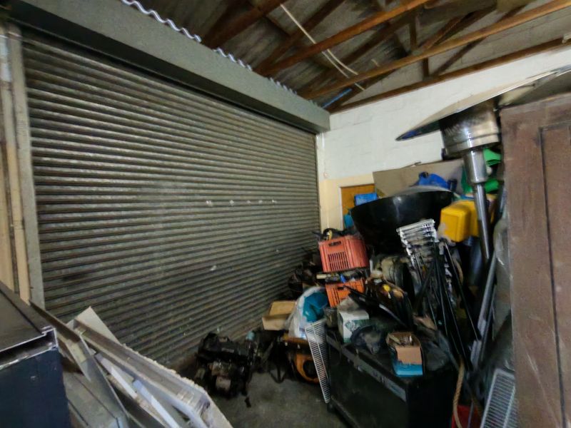 Industrial garage space featuring a large roller shutter door, exposed timber roof structure, and concrete flooring.