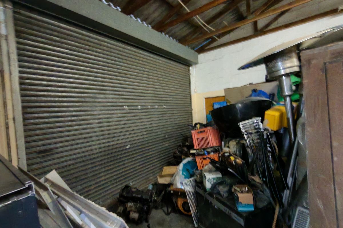 Industrial garage space featuring a large roller shutter door, exposed timber roof structure, and concrete flooring.