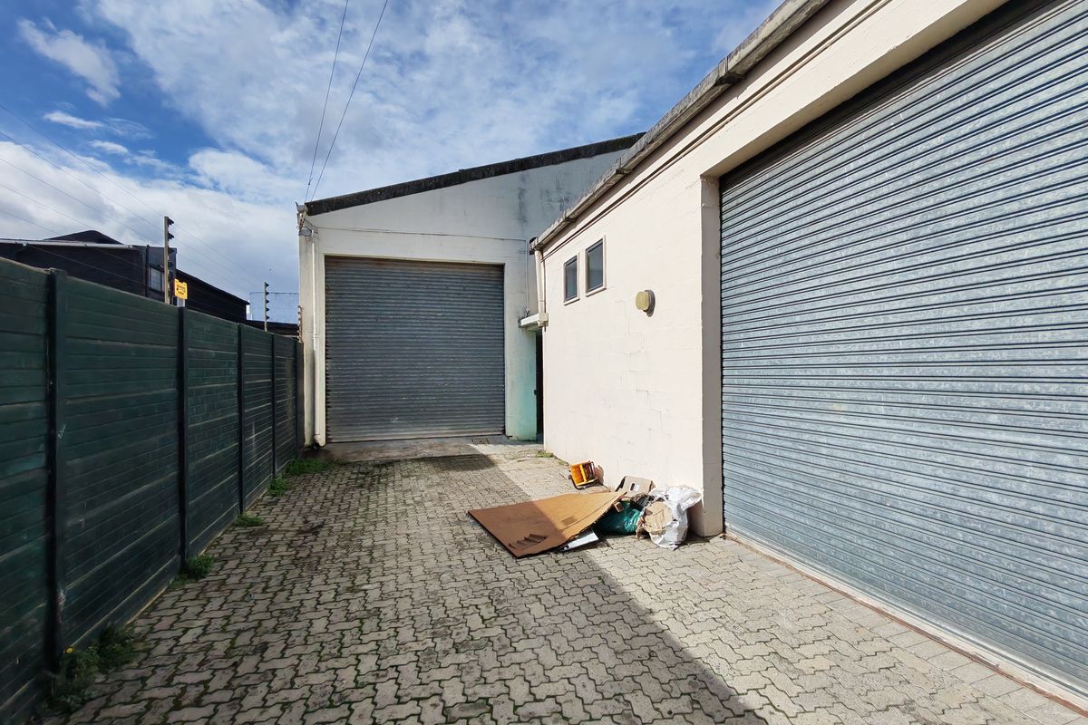 Rear exterior view of an industrial property featuring paved access, secure roller shutter doors, and perimeter fencing.