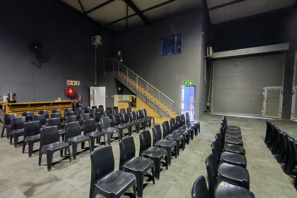 Large industrial utility space featuring high ceilings with exposed steel trusses, a roller shutter door, and an internal staircase leading to an upper level.