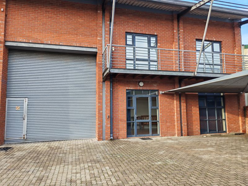 Industrial property exterior featuring a large roller shutter door, brick facade, and a steel balcony with paved driveway access.